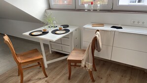 Una cocina moderna con una mesa de comedor, dos sillas de madera, un banco y una pequeña isla con tabla de cortar.