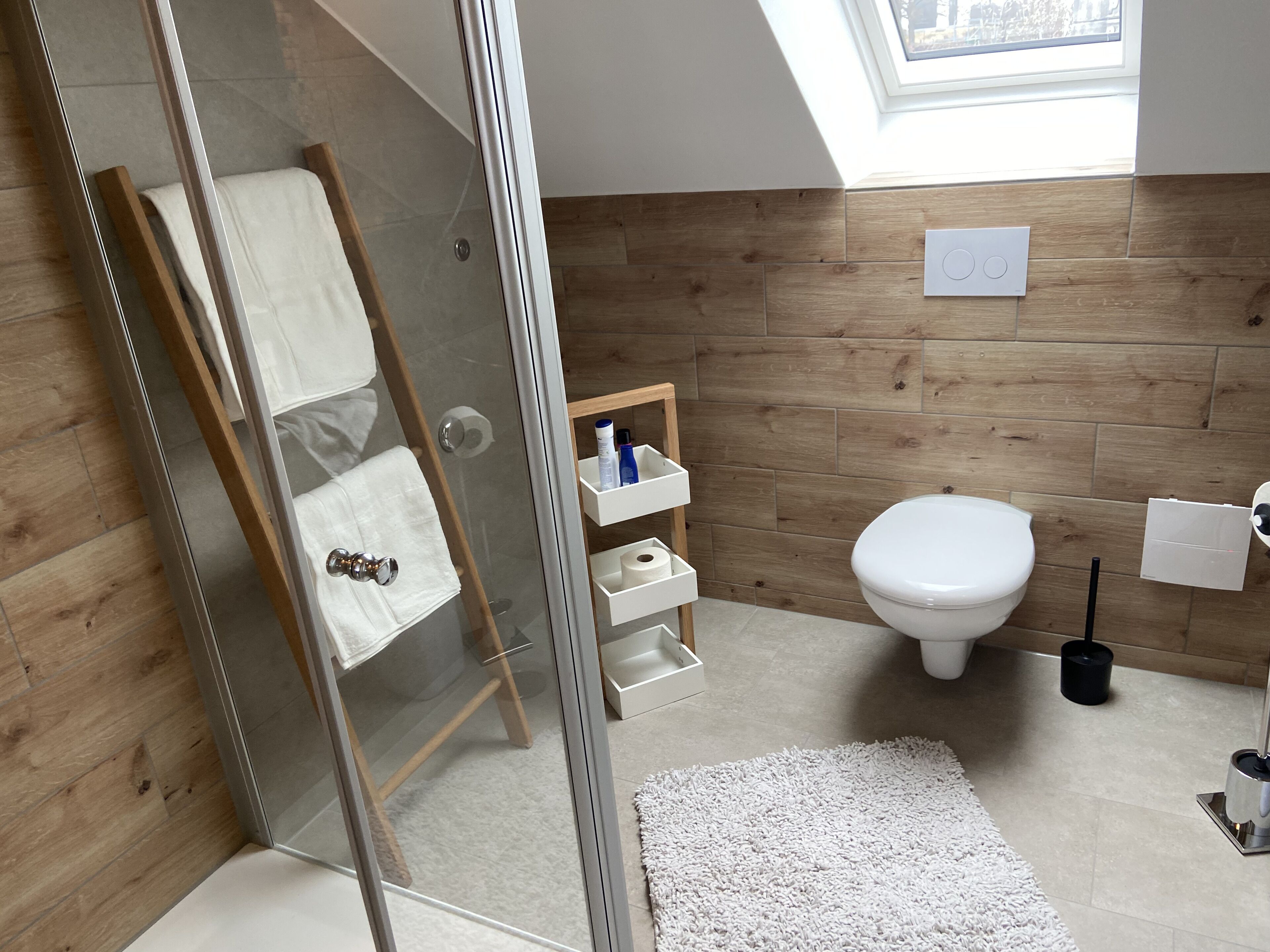 Une salle de bain moderne avec une douche à parois de verre, un meuble-lavabo en bois, des toilettes et une petite étagère contenant des articles de toilette.