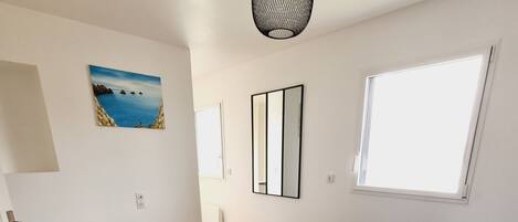 A bedroom with a large bed, a window, a painting, and a hanging light fixture.