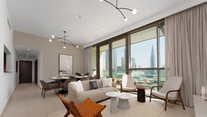 A modern living room with a sofa, coffee table, and chairs, a dining area with a table and chairs, and large windows with a city view. - Maison Privee - Luxury Apt with Burj Khalifa Vw & Direct Mall Access (Dubai)