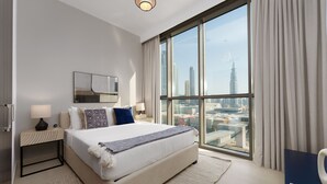 A modern hotel room with a large bed, a nightstand, a lamp, and a view of a cityscape through large windows. - Maison Privee - Luxury Apt with Burj Khalifa Vw & Direct Mall Access (Dubai)