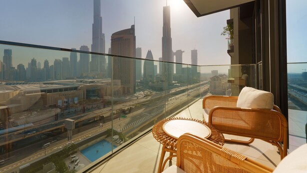 A balcony with wicker furniture, a glass railing, and a view of a cityscape including the Burj Khalifa. - Maison Privee - Luxury Apt with Burj Khalifa Vw & Direct Mall Access (Dubai)