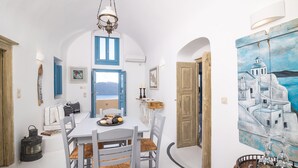 Zona pranzo con tavolo bianco, persiane blu e vista sul mare.