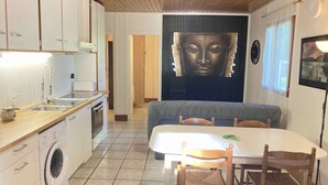 Una cocina compacta con lavadora, un comedor con mesa y sillas, y una gran estatua de Buda en la pared.