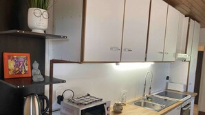 Una cocina compacta con armarios blancos, un microondas, una tetera y un lavabo.
