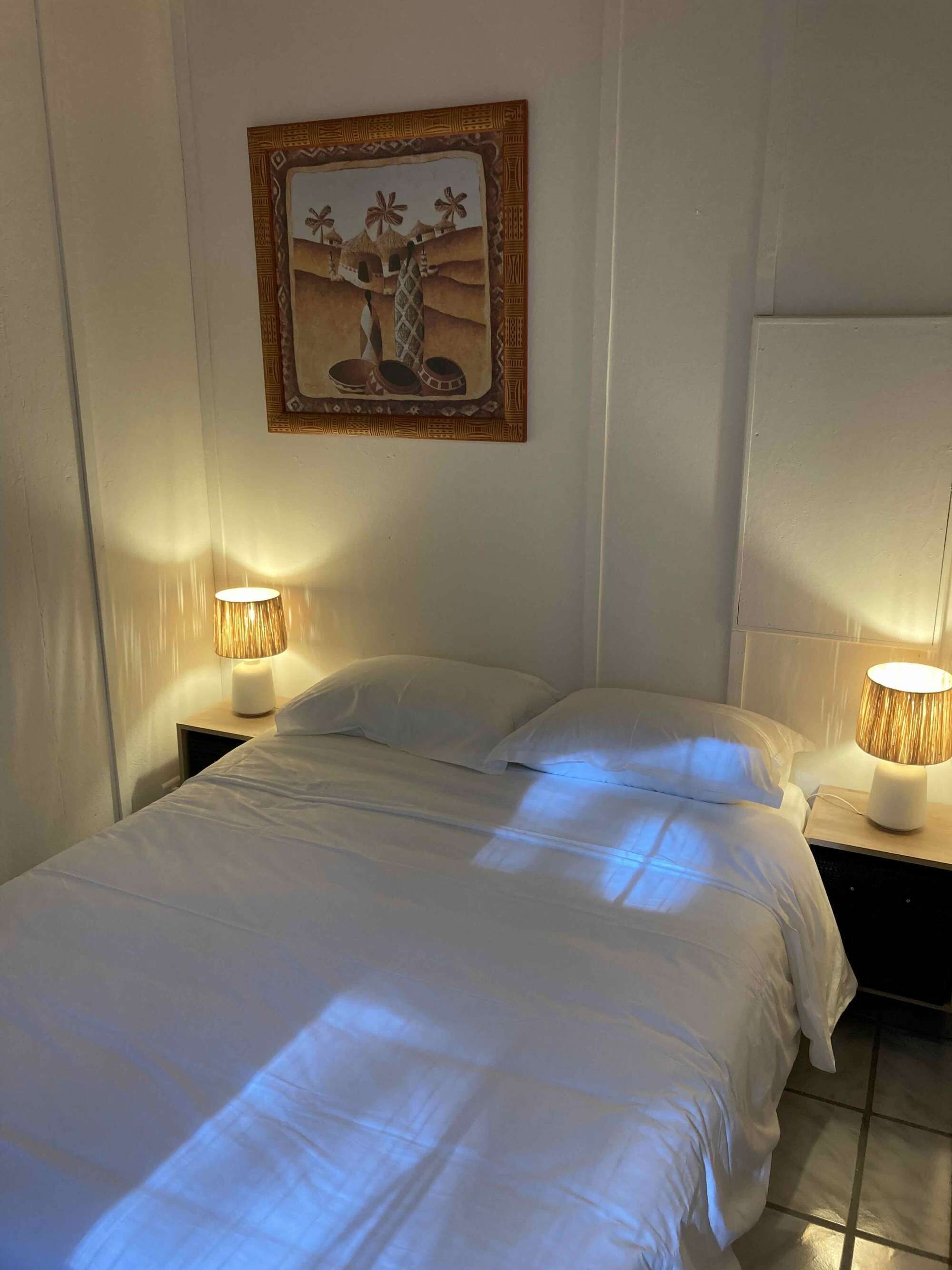 A hotel room with two beds, a framed picture on the wall, and two bedside lamps.