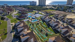 Vue aérienne d’un quartier résidentiel avec des maisons, une piscine et une plage.