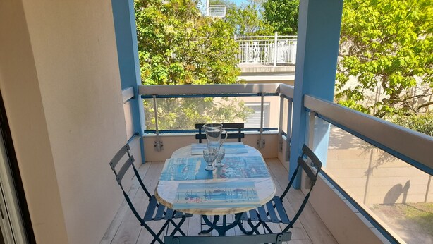 A balcony with a table and chairs, a view of trees and a building in the background. - Arcachon: Central T2, Close to Casino, Beach & Shops, Private Parking (Arcachon)