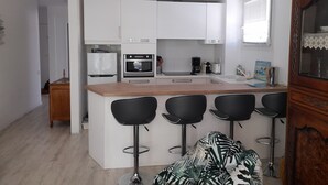 A modern kitchen with white cabinets, a central island with bar stools, a refrigerator, an oven, and a coffee maker. - Arcachon: Central T2, Close to Casino, Beach & Shops, Private Parking (Arcachon)