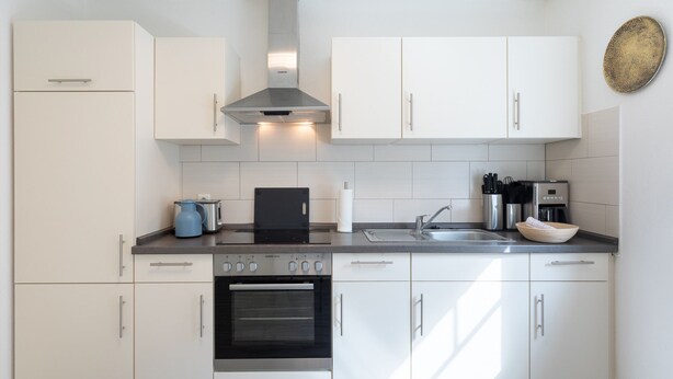 A modern kitchen with white cabinets, a stainless steel range hood, a built-in oven, a coffee maker, and a kettle on the countertop. - Vacation apartment Achterdeck in Drelsdorf for up to 4 people (Drelsdorf)