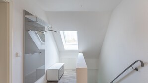 A modern, minimalistic stairwell with a glass door leading to a bathroom, a small window providing natural light, and a white bench. - Vacation apartment Achterdeck in Drelsdorf for up to 4 people (Drelsdorf)