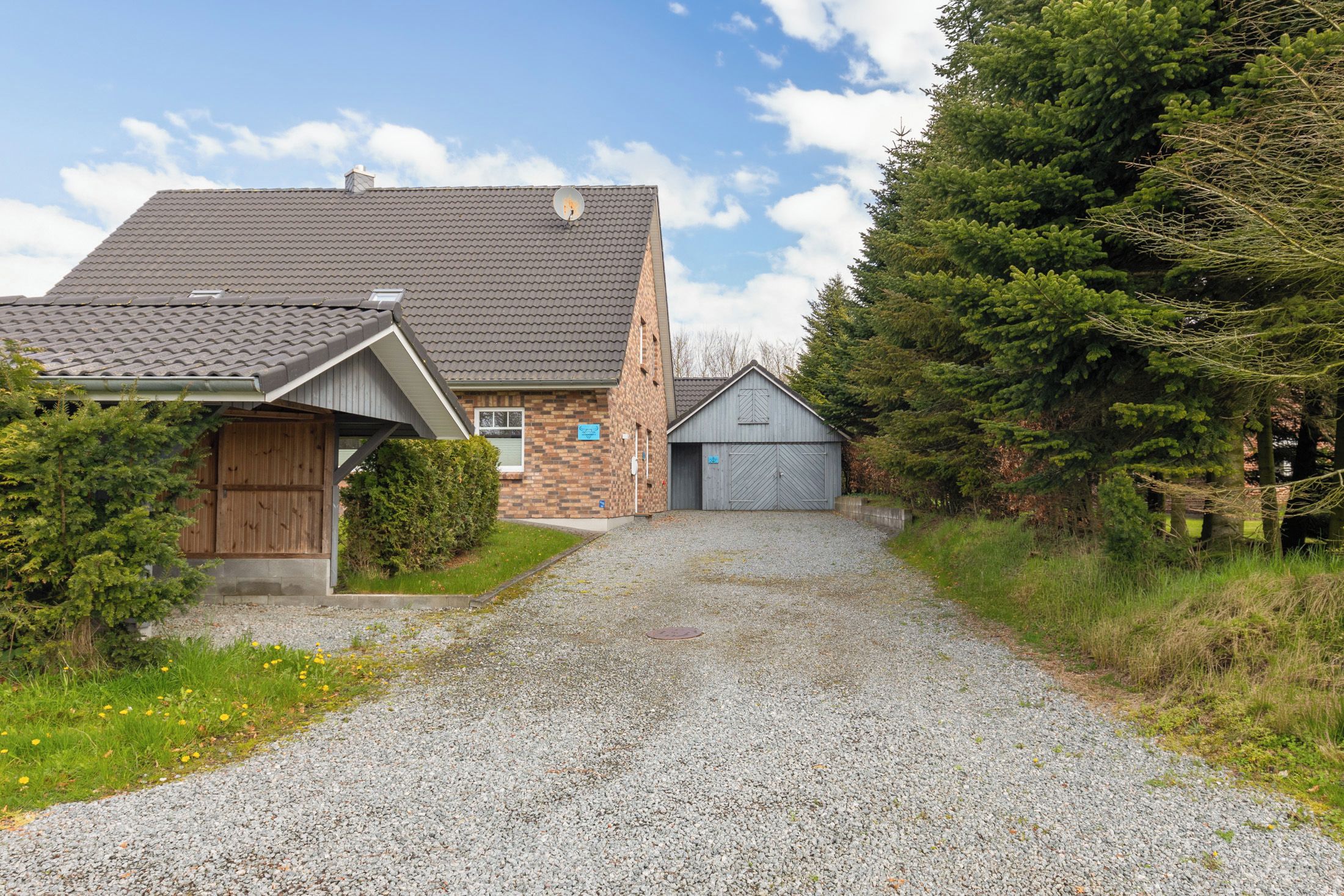 Ein Kiesweg führt zu einem Haus mit Garage und Gartenhaus.