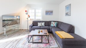 A modern living room with a grey sofa, a coffee table, and a TV on a glass stand. - Vacation apartment Achterdeck in Drelsdorf for up to 4 people (Drelsdorf)