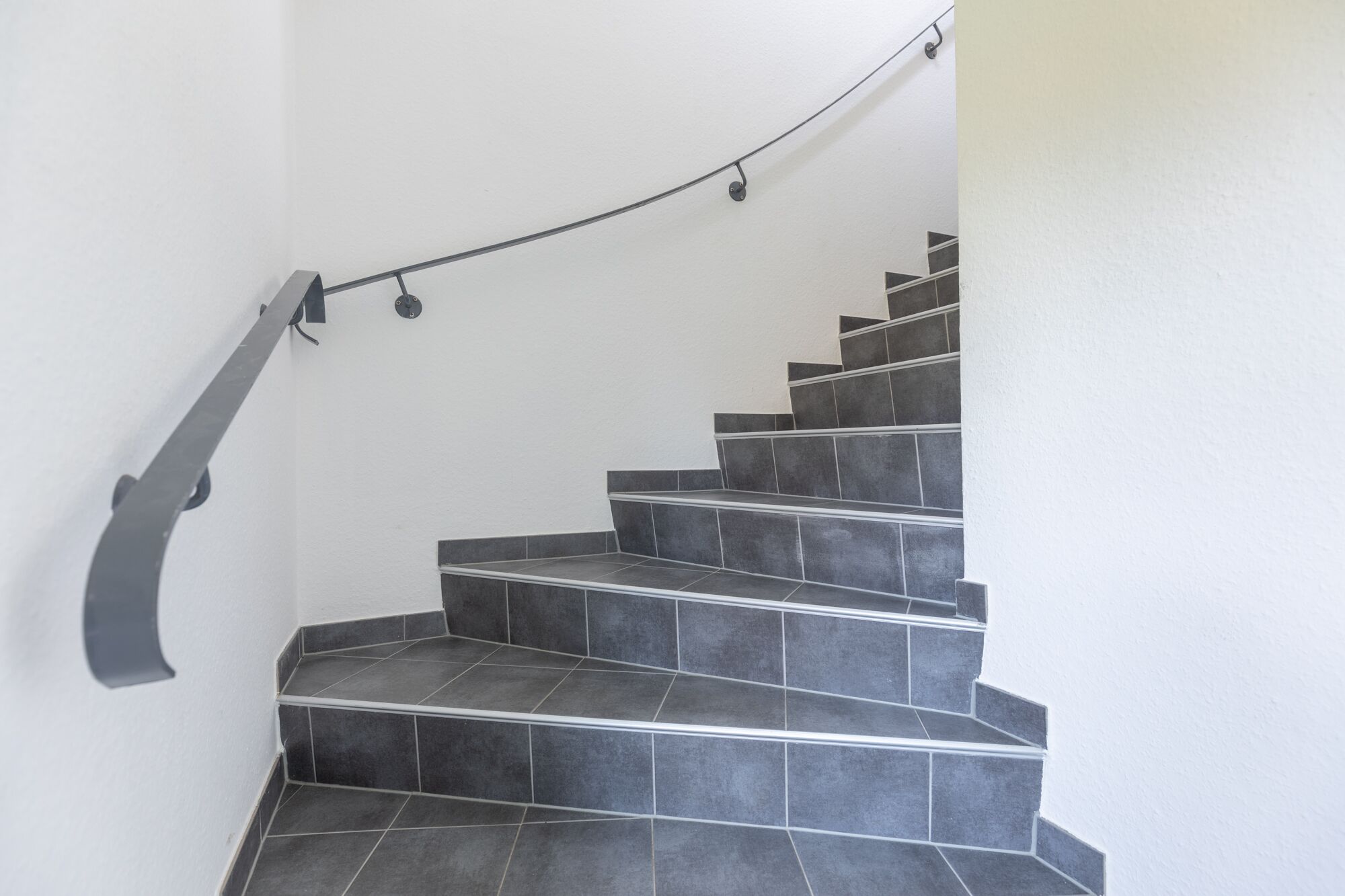 Eine Treppe mit dunkelgrauen Fliesen und einem Metallgeländer.