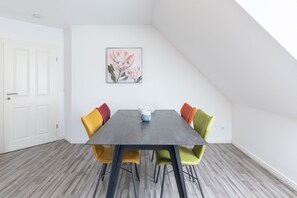 Ein Essbereich mit einem dunklen Tisch, bunten Stühlen und einem gerahmten Blumenbild an der Wand.