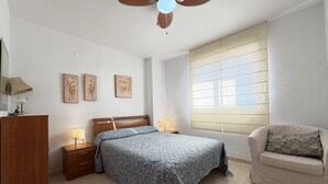 Een slaapkamer met een bed, nachtkastjes, een kledingkast, een raam met zonwering en een plafondventilator.