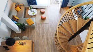 Ein modernes Interieur mit einer Wendeltreppe aus Holz, einer Couch mit bunten Kissen, einem Esstisch mit Stühlen und einem kleinen weißen Tisch mit einer Vase.
