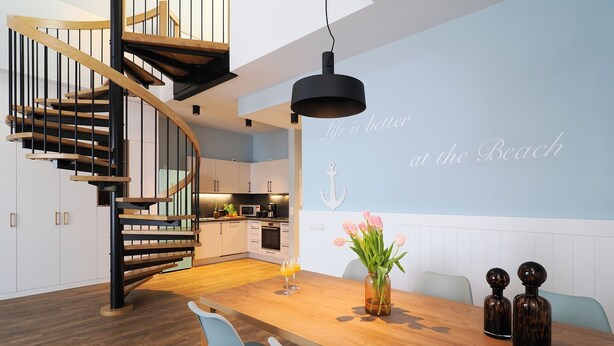 Eine moderne Küche mit einer Wendeltreppe, einem Essbereich mit einem Holztisch und einer Wand mit einem nautisch gestalteten Wandbild.