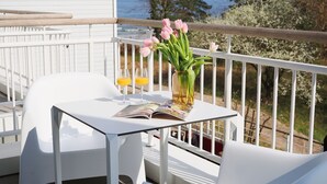 Une table blanche avec deux chaises sur un balcon, un vase rempli de fleurs roses et deux verres de jus d’orange.