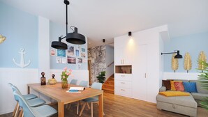 A modern living room with a wooden dining table, light blue chairs, a grey sofa, and a staircase leading to an upper level. - Vacation apartment with 1 bedroom and balcony facing the lake (Seebad Heringsdorf)
