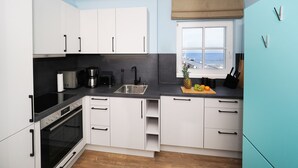 A modern kitchen with white cabinets, a black countertop, and a view of the sea through a window. - Vacation apartment with 1 bedroom and balcony facing the lake (Seebad Heringsdorf)