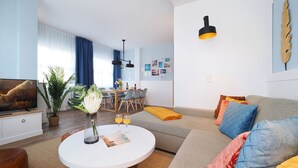 A modern living room with a sofa, coffee table, and a dining area with chairs and a table. - Vacation apartment with 1 bedroom and balcony facing the lake (Seebad Heringsdorf)