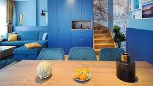 Ein modernes Wohnzimmer mit einem blauen Sofa, einem Esstisch mit Obst und einer Treppe.