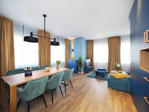 A modern living room with a wooden dining table, teal chairs, a blue sofa, and a blue cabinet.