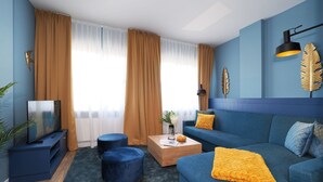 Ein modernes Wohnzimmer mit einem blauen Sofa, zwei runden Hocker, einem Fernseher auf einem Schrank und einem Couchtisch.