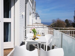 Ein Balkon mit weißen Stühlen und einem Tisch, einer Blumenvase und zwei Gläsern Orangensaft.