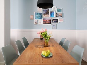 Ein Esszimmer mit einem Holztisch, sechs Stühlen, einer Blumenvase und einem Teller mit Äpfeln.