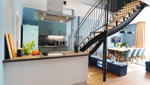 Una cucina moderna con isola centrale, zona pranzo con scala e salotto con divano e tavolino.