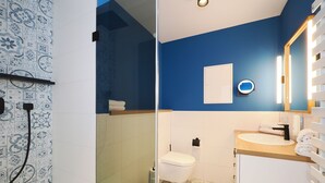 Een badkamer met een blauwe accentmuur, een witte wastafel, een spiegel met verlichting en een toilet.