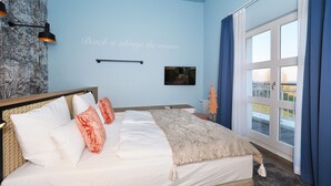 Een slaapkamer met een bed, een wandplank, een schilderij en uitzicht door een raam.