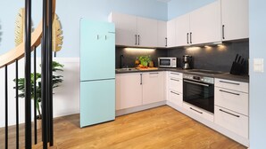 Una cocina moderna con armarios blancos, un refrigerador azul claro, microondas, cafetera y suelo de madera.