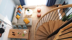 Un interior moderno con una escalera espiral, un conjunto de sofás, una mesa de comedor y una pequeña mesa redonda con una planta.