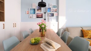 Un comedor con una mesa de madera, sillas, un florero con flores, un plato de manzanas y uvas, y un libro.