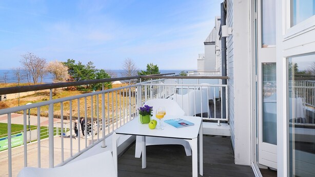 En balkon med et hvidt bord, to hvide stole, en potteplante og et glas appelsinjuice.