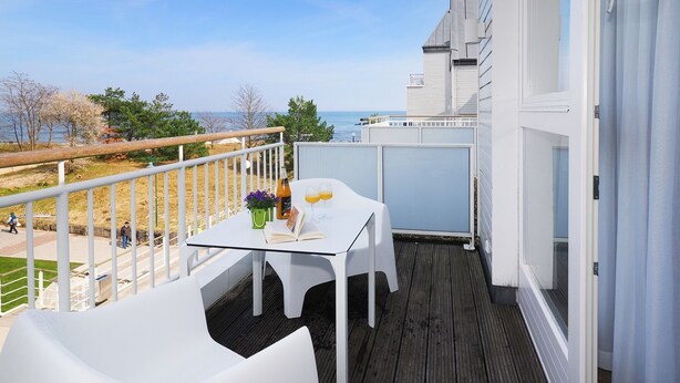 A balcony with a white table, two white chairs, a bottle of orange juice, and a book. - 1-room vacation apartment with balcony (Seebad Heringsdorf)