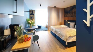 A modern hotel room with a bed, a desk with a toaster, a chair, a small table with fruits, and a decorative wall. - 1-room vacation apartment with balcony (Seebad Heringsdorf)