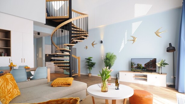 Een moderne woonkamer met een spiltrap, een bank, een salontafel en een televisie.