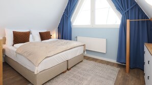Een slaapkamer met een bed, een radiator, een raam met blauwe gordijnen en een houten garderobe.