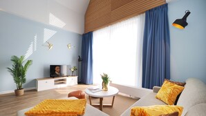 Een moderne woonkamer met een bank, een salontafel en een televisie. Gordijnen, een lamp en een plantje zijn aanwezig.