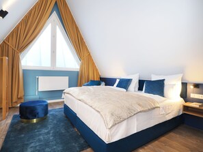 Une chambre avec un grand lit, une fenêtre avec des rideaux, un radiateur et un petit pouf.