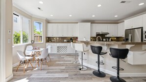 A modern kitchen with white cabinets, a stainless steel refrigerator, and a dining area with white chairs and a table. - 5BR Home Modern & Spacious for Business & Family (San Jose)