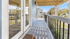 A covered porch with a wooden railing and a door leading to a room. - Fenwick Shores House II (Selbyville)