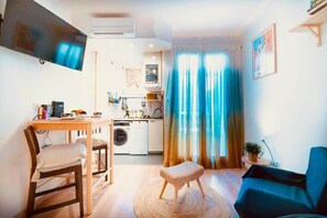 A compact living space with a dining area, kitchenette, and a TV mounted on the wall.
