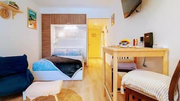 A compact room with a bed, a small table, a chair, a sofa, and a television mounted on the wall.
