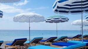 Ein Strand mit Liegestühlen und gestreiften Sonnenschirmen.