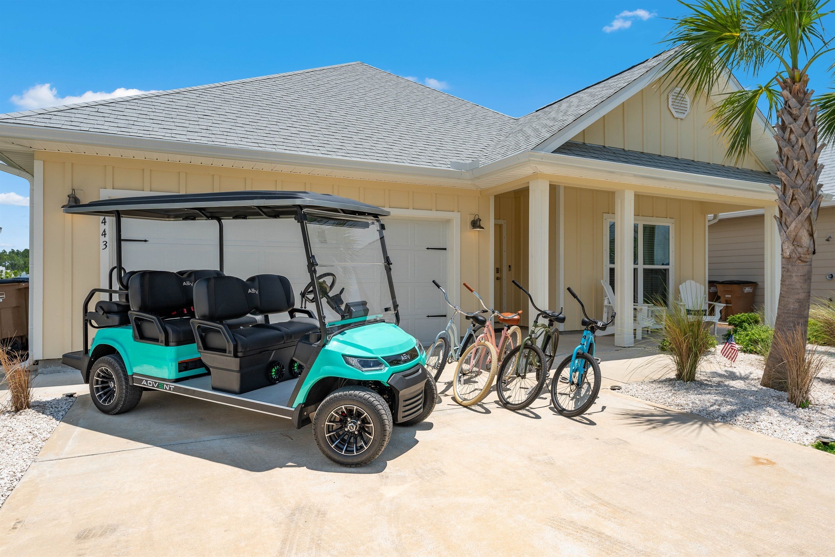 A golf cart parked in front of a house with a garage, a bicycle, and a palm tree.